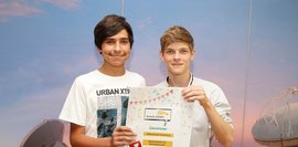 Zwei Schüler, vor einer blauen Wand, die ein Plakat in der Hand halten und für ein Foto posieren