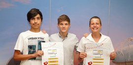 Drei Schüler, vor einer blauen Wand, die ein Plakat in der Hand halten und für ein Foto posieren