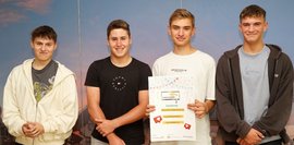 Vier Schüler, vor einer blauen Wand, die ein Plakat in der Hand halten und für ein Foto posieren