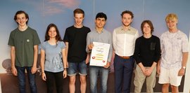 Eine Gruppe von Schülern, vor einer blauen Wand, die ein Plakat in der Hand halten und für ein Foto posieren