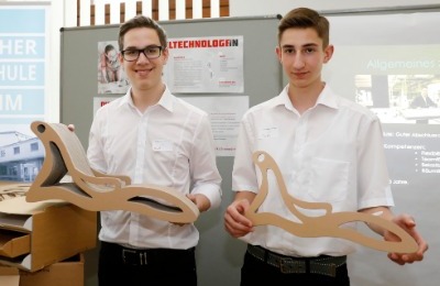 Zwei Schüler, die jeweils eine Liege aus Pappe in Miniaturgröße in der Hand halten