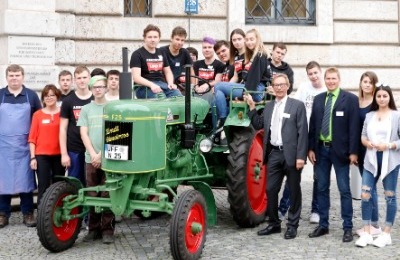 Eine große Gruppe aus Erwachsenen und Schülern, die um einen Traktor herum stehen und teilweise darauf sitzen und für ein Foto posieren