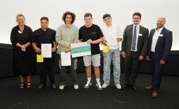 Vier Schüler, die Plakate in der Hand halten und mit drei Erwachsenen für ein Foto posieren