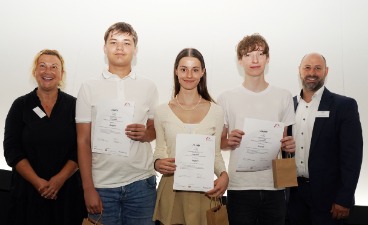 Zwei Schüler und eine Schülerin, die Plakate in der Hand halten und mit zwei Erwachsenen für ein Foto posieren