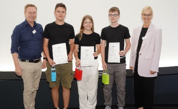 Die Gewinner des Praxispreises Eine Schülerin und zwei Schüler, die Plakate in der Hand halten und mit zwei Erwachsenen für ein Foto posieren